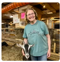 Mary smiling beside a goat inside a wooden barn.