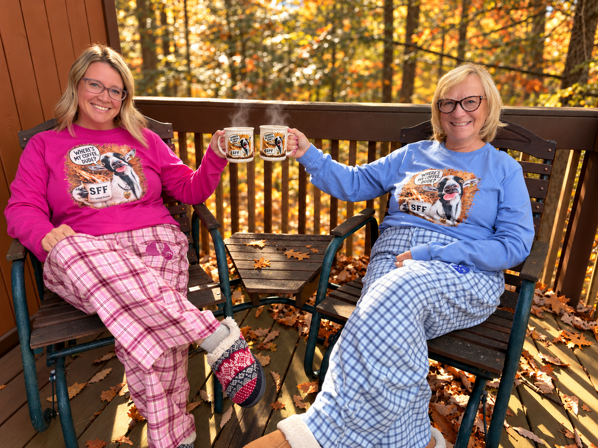 Two women in pink and blue Pep long-sleeve shirts and SFF plaid pajama pants sharing coffee on a cozy autumn cabin porch.